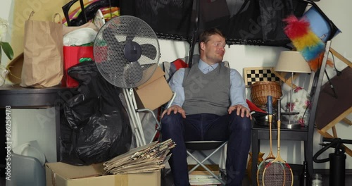 compulsive hoarding disorder concept - man hoarder sitting in the chair and looking on his stuff piles photo