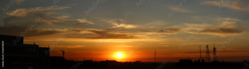 Color photograph of the city against the sunset. The Yellow Sun sets over the horizon. Beautiful clouds in the sky. Smooth natural gradient from blue to red. End of the day.