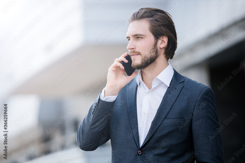Stylish young businessman with a beard is talking on the phone in the city against the background of modern buildings Stylish young businessman with a beard is talking on the phone in the city against the background of modern buildings