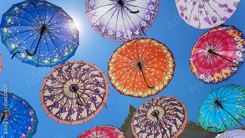 Coloful umbrellas with paterns on blue sky background with sun glare. Buddhist temple in Hua Hin, Thailand.