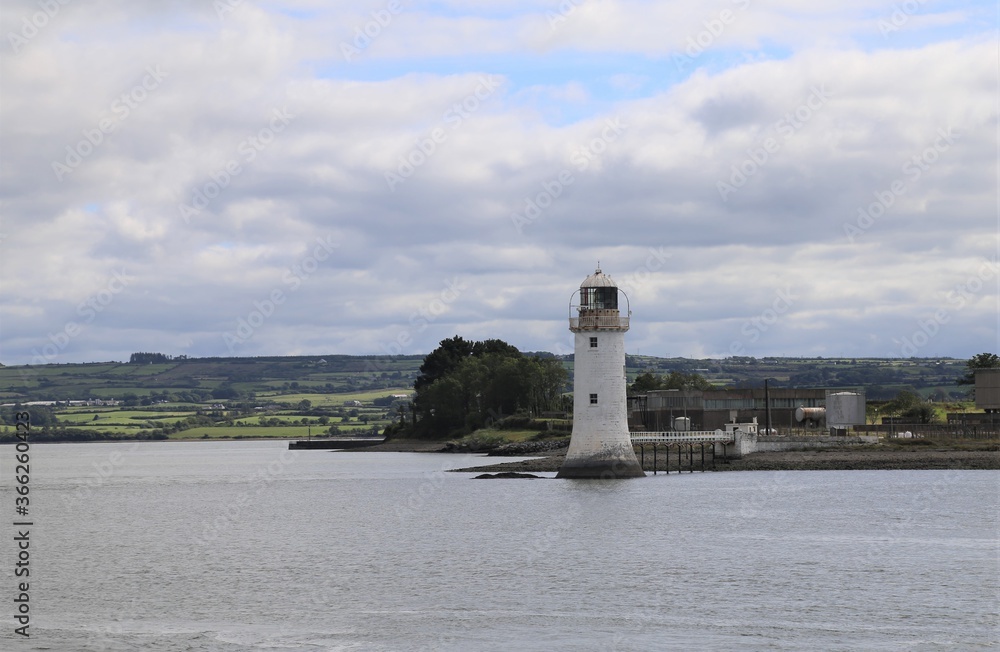 The small, white harbour lighthouse on the Shannon Estuary with the landscape of County Kerry, Ireland in the background. The small, white harbour lighthouse on the Shannon Estuary with the landscape of County Kerry, Ireland in the background.