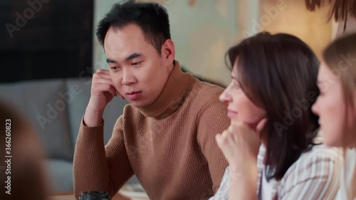 Young handsome stressed Asian manager businessman is bored and tired of sitting at busy office workplace team meeting.