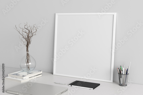 Square poster frame mockup on the white table of home studio workspace with white wall. Side view, clipping path around poster picture.