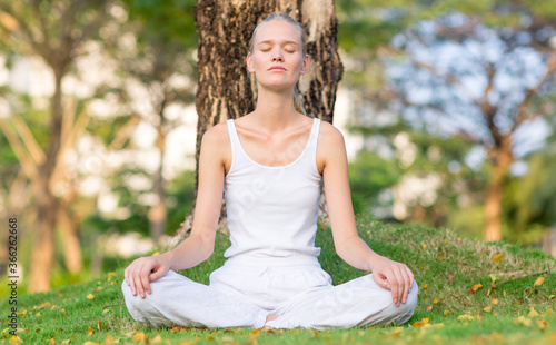 Wallpaper Mural Serene young woman meditating outdoor at peace on the grass under a tree at the park on a calm morning. Self care, mind and body relaxation. Torontodigital.ca