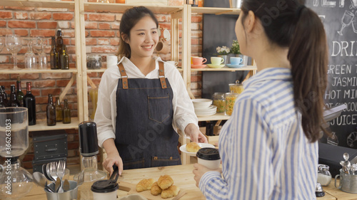 Barista serving cup of coffee to go and delicious croissant for customer at counter in small cafe shop. female owner serving breakfast to client in coffeehouse. waitress smiling to office lady guest