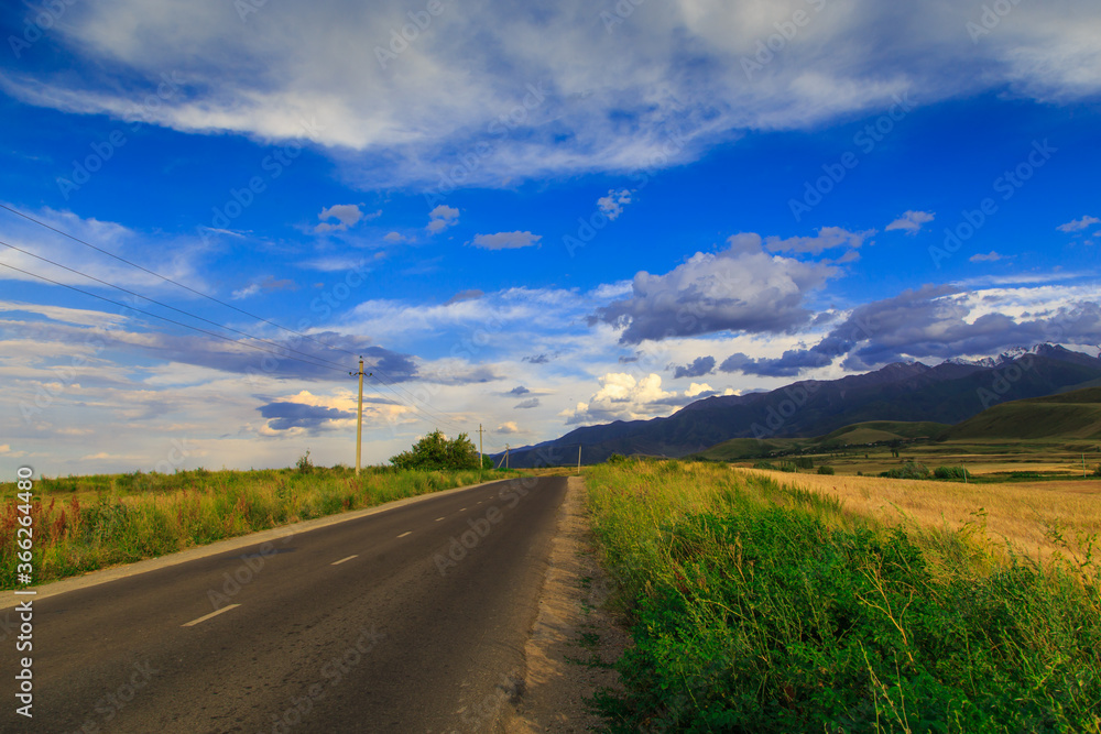 Beautiful summer landscape. Mountain country road among green hills. Lush green hills, high mountains. Spring flowering grass. Beautiful summer landscape. Mountain country road among green hills. Lush green hills, high mountains. Spring flowering grass.