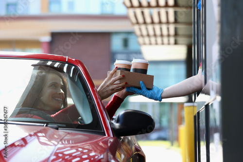 Woman in convertible car picks up tea and coffee in Mcdrive. Fast and safe service in restaurants and cafes concept
