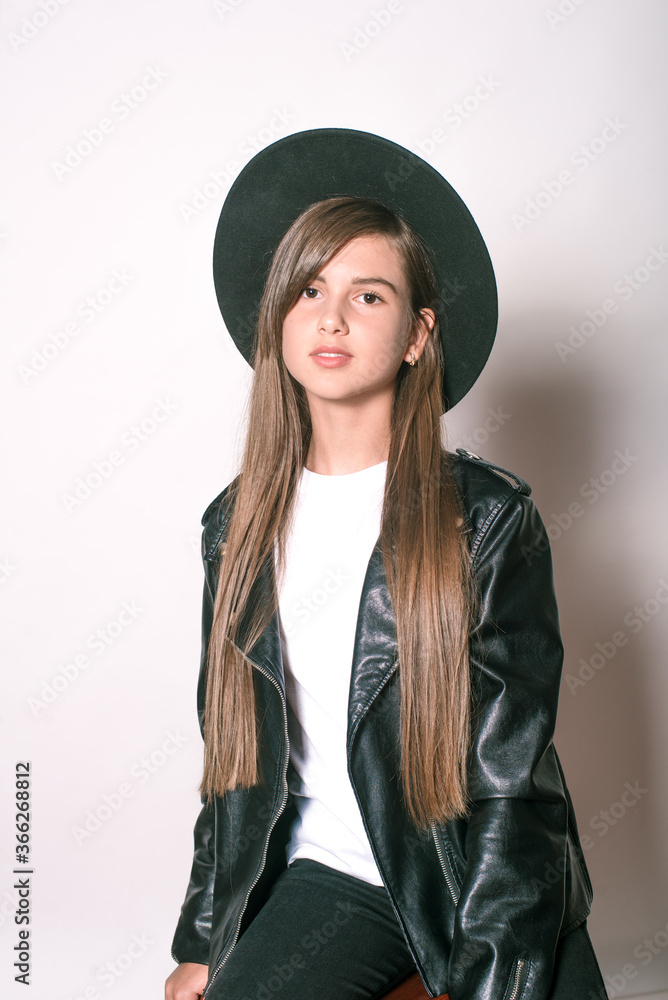A teenage girl in a trendy leather jacket and an even hat on a white background. Teenage fashion. Street fashion. Beauty and fashion
