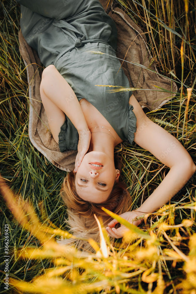 Luxury blonde in a green suit lies between ears of wheat in a field during sunset Luxury blonde in a green suit lies between ears of wheat in a field during sunset