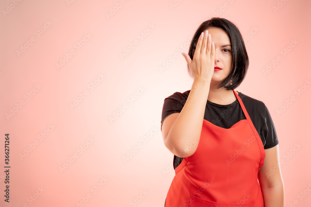 Woman employed at supermarket with red apron and black t-shirt cover one eye Woman employed at supermarket with red apron and black t-shirt cover one eye