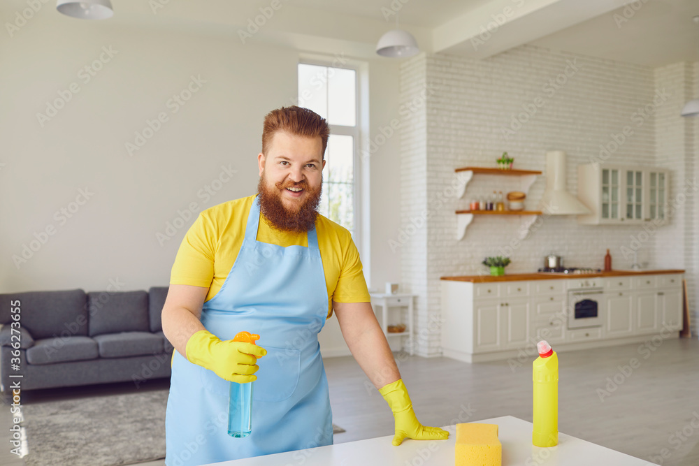 Funny fat man with a beard in an apron cleans the room in the house. Funny fat man with a beard in an apron cleans the room in the house.