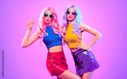 Fashion. Disco party woman have fun dance. Two DJ girl in colorful neon light, sisters. Beautiful model, stylish hair, 80s 90s neon nightclub fashionable style. Pop art. Creative neon light