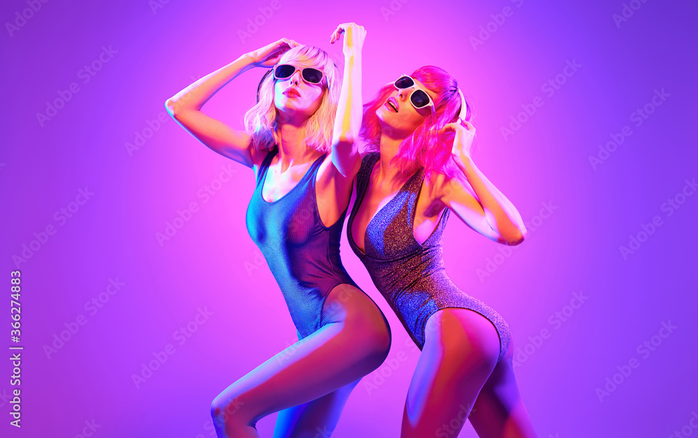 Fashion. Two DJ girl in Colorful neon light enjoy music, friends. Party disco 80s 90s neon nightclub vibes. Model woman in disco bodysuit, makeup dance. Creative art neon light