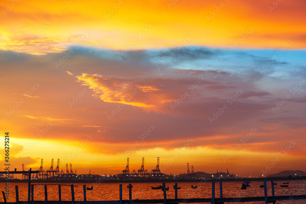 Fototapeta premium cranes on seaport and sunset red blue sky and fishing boats on sea