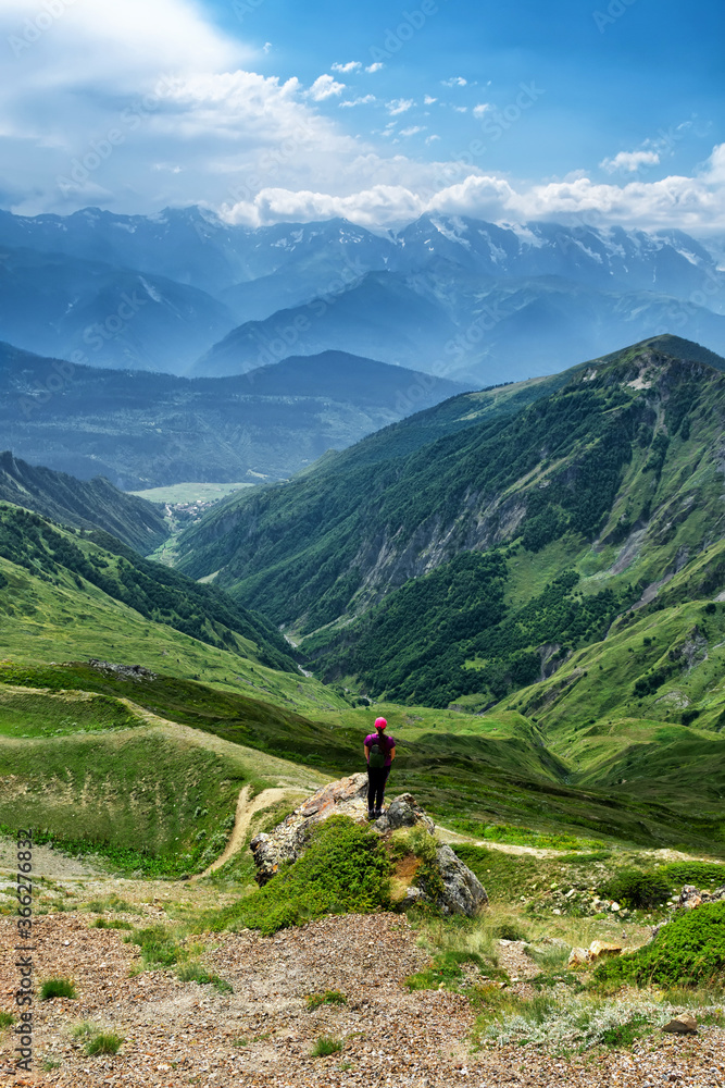 A girl in a hat stands on a stone on the background of the Svaneti. Caucasus mountains in summer