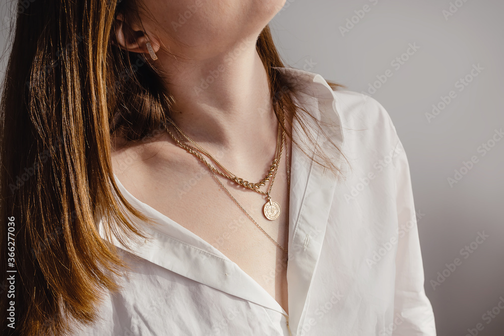 Close-up young woman in white shirt wearing golden necklaces. imalist lifestyle