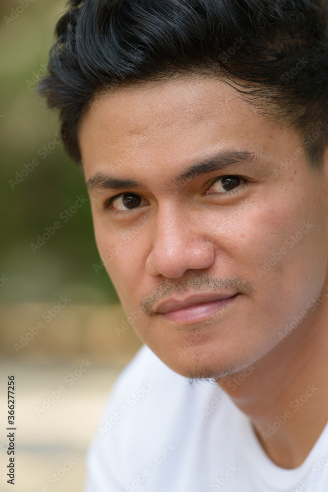 Face of handsome Asian man looking at camera outdoors Face of handsome Asian man looking at camera outdoors