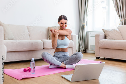 Girl training at home, doing workout and watching videos on laptop, training in living room. She is watching video on the internet and repeating the tasks