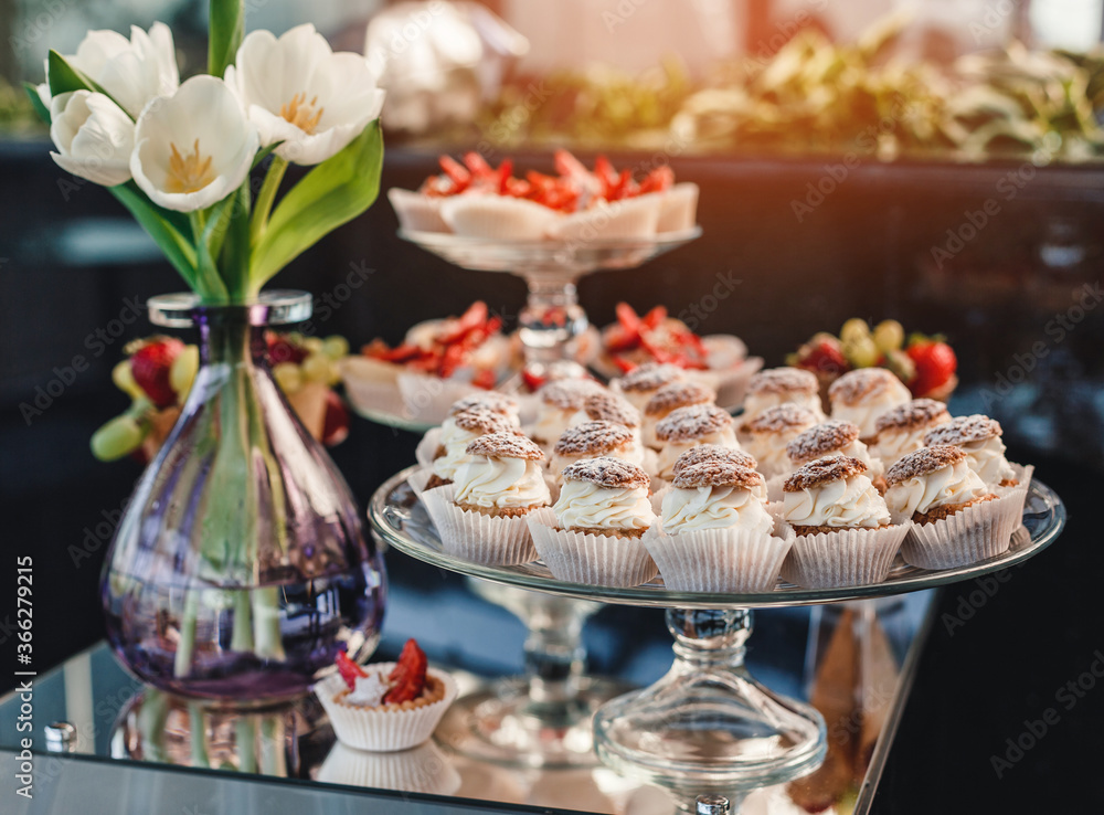 Wedding dessert, macaroons, meringues, cupcakes, muffins, cakes and sweetness on holiday background with flowers. Candy bar