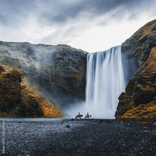 Impressively beautiful nature of Iceland during sunset. Skogafoss waterfall is one famous natural landmark and travel destination place of Iceland. Tourists ride horses near famouse waterfall. photo