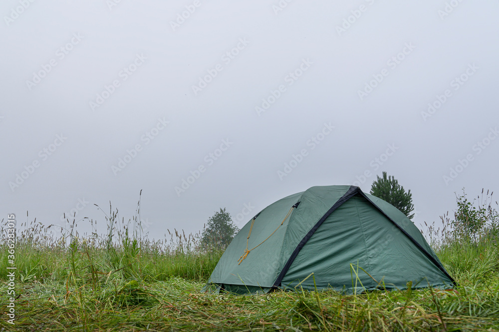 a green camping tent stands on the grass. morning, heavy fog. tourism and Hiking