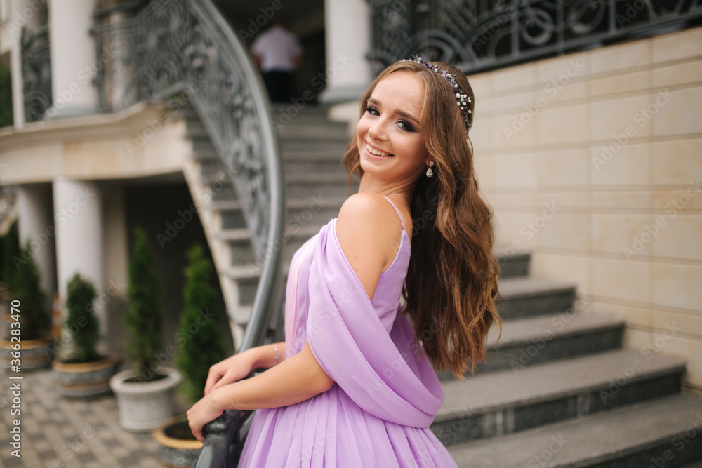 Fototapeta premium Portrait of elegant woman in purple evening dress walking outdoors by restaurant