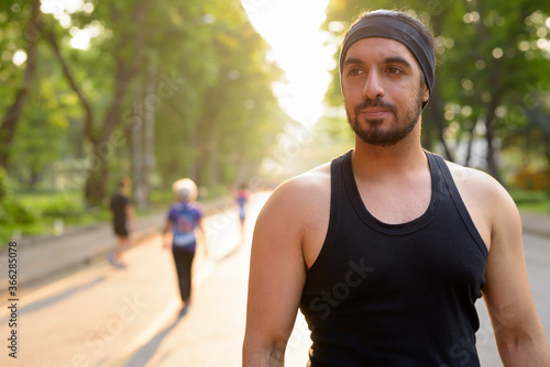 Young handsome bearded Indian man with headband thinking at the park