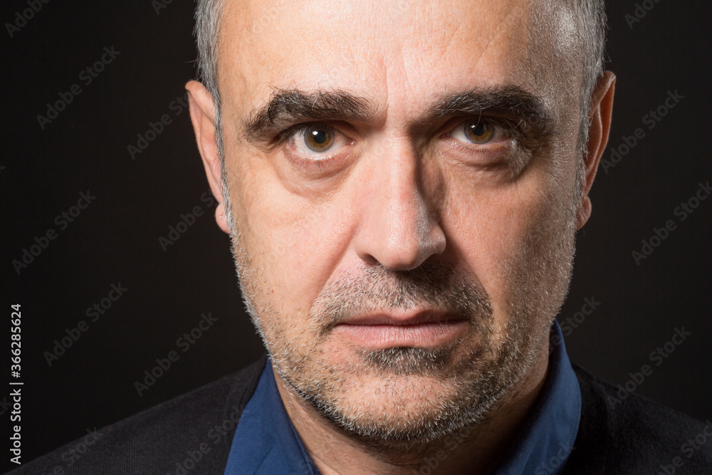 Fototapeta premium Ritratto stretto di un uomo che guarda con espressione dura e severa isolato nell'oscurità