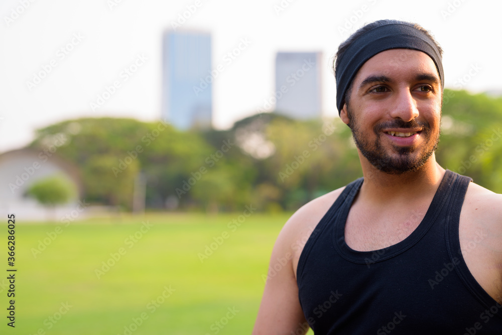 Face of happy young handsome bearded Indian man thinking at the park Face of happy young handsome bearded Indian man thinking at the park
