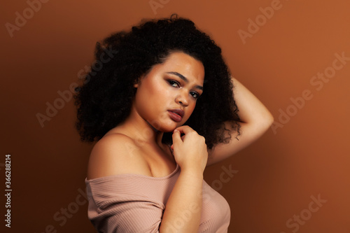 pretty young african american woman with curly hair posing cheerful gesturing on brown background, lifestyle people concept