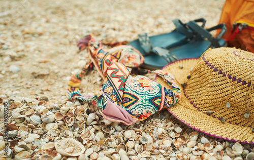 Close-up woman vacation set, beach accessories on seashells. Summer concept of beach, straw hat, bikini and sandals