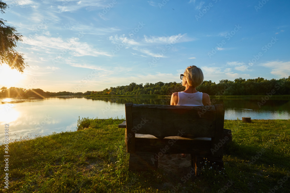 Fototapeta premium Woman Sitting On Bench During A Beautiful Sunset