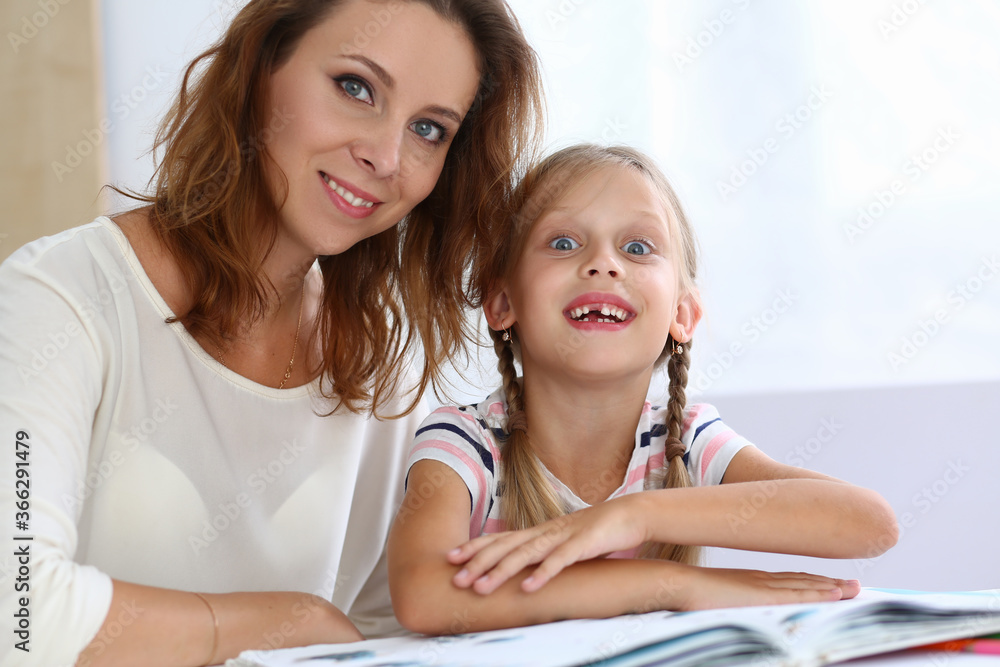 Portrait of cheerful woman with her child while they are sitting at table and reading book Portrait of cheerful woman with her child while they are sitting at table and reading book