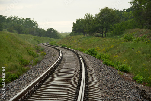 Railroad meanders among green slopes summer day