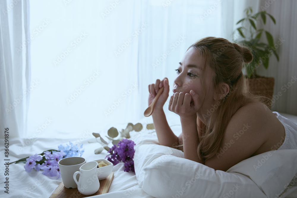 爽やかな朝に寝室のベッドでくつろぐ白いワンピースの女性