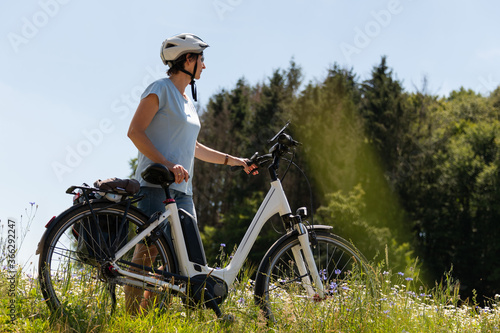 Fahrrad Fahrerin schiebt an einem schönen Sommertag ihr Fahrrad durch eine blühende Sommerwiese.