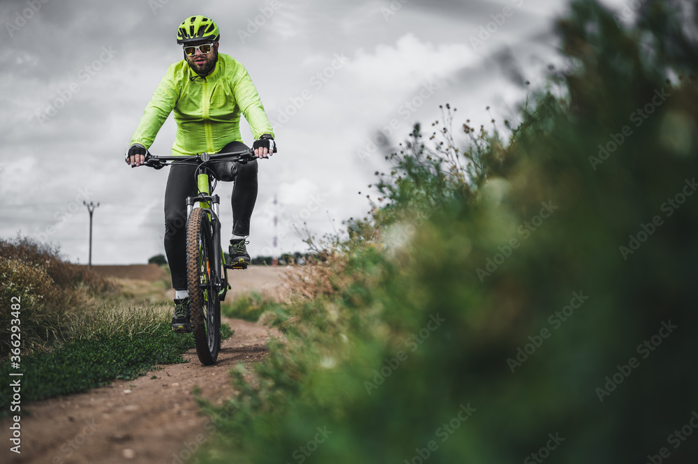 Naklejka premium Cyclist riding a bike on the road. Nature and recreation. Hobbies and sports. Cyclist on summer ride. Dark clouds background.