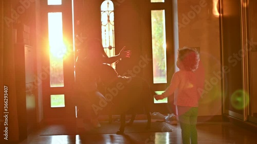 A child meets mom from work. The girl joyfully runs to the front door, where her mother enters, Backlight, camera moves