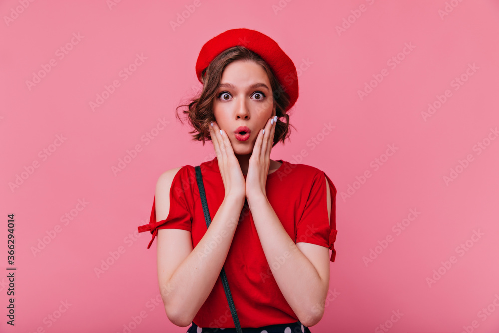 Fototapeta premium Dark-eyed french woman expressing amazement. Studio portrait of surprised glamorous girl in red beret.