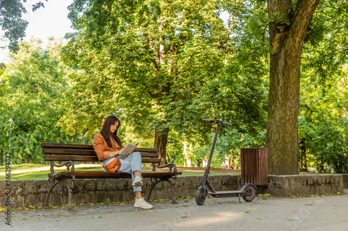 A young woman is sitting on a park bench with the book in her han © MexChriss