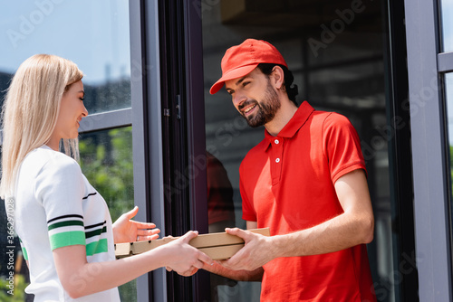 Smiling waiter giving pizza boxes to woman near cafe on urban street