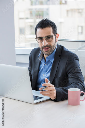 manager vestito con giacca nera e camicia blu, seduto nella sua postazione di lavoro si concentra nello scrivere qualcosa nella tastiera del suo portatile