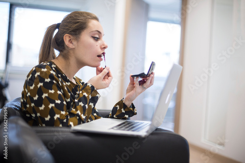 Ragazza bionda con i capelli raccolti vestita casual si trucca durante l'orario di lavoro nel suo ufficio  photo