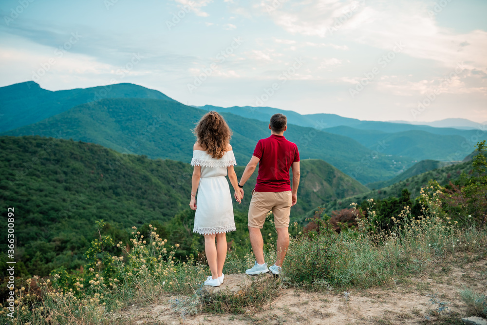 Romantic traveling couple walking in the mountains. Caucasian man and woman in love in mountains at sunset. Portrait of a happy couple smile back to camera. Lifestyle concept.