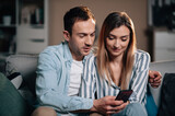 Portrait of young couple at home on sofa with cellphone