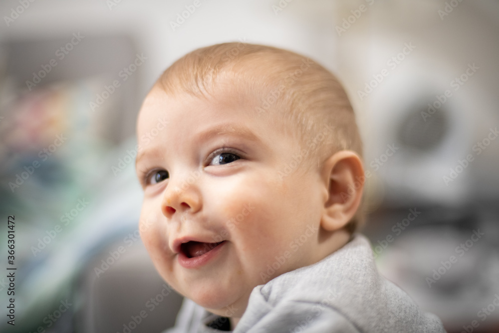 Retrato de bebé rubio sonriendo y mirando hacia la cámara cerca de una ventana