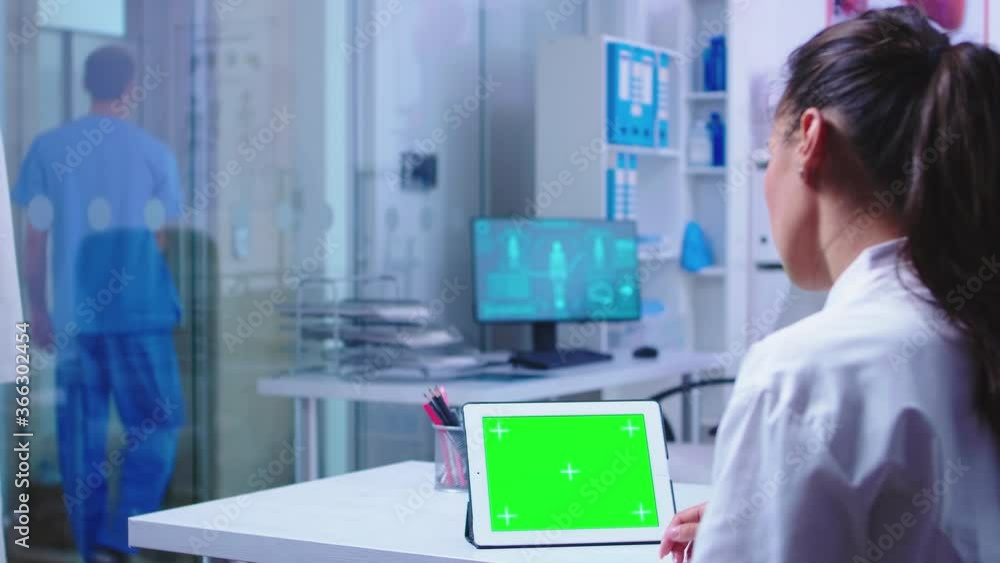 Medic reading on tablet pc with green screen in hospital cabinet about a dangerous virus. Assistant in blue medical uniform. Doctor in health clinic working on tablet computer with replaceable screen Medic reading on tablet pc with green screen in hospital cabinet about a dangerous virus. Assistant in blue medical uniform. Doctor in health clinic working on tablet computer with replaceable screen