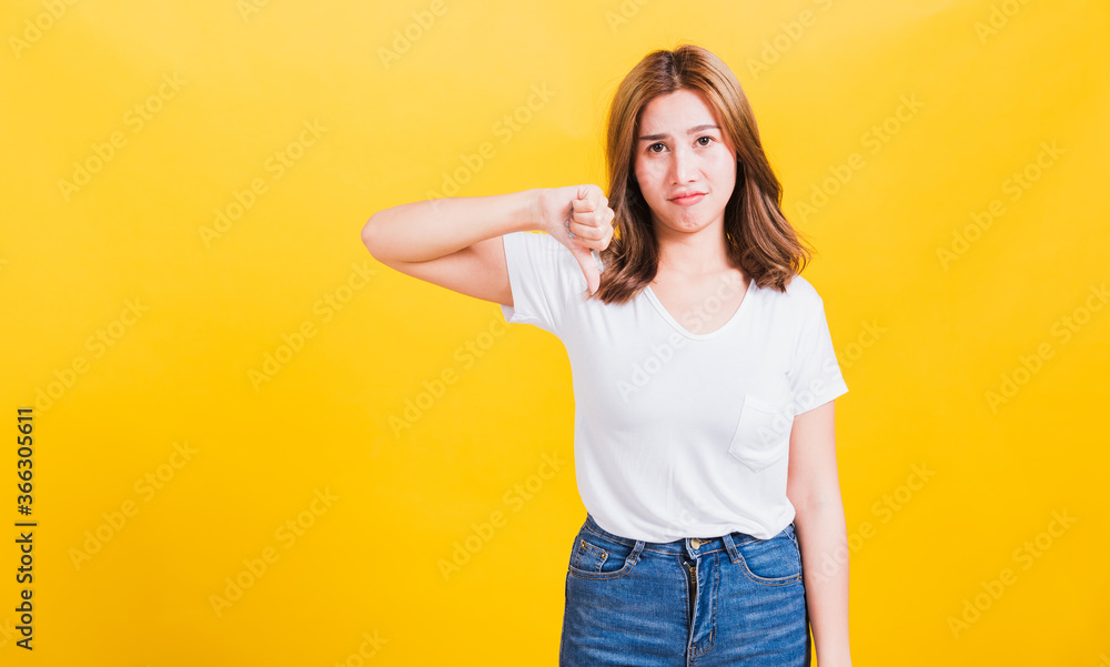 Portrait Asian Thai beautiful young woman unhappy, a negative gesture showing finger thumbs down or dislike sign, studio shot isolated on yellow background, There was copy space, rejection concept Portrait Asian Thai beautiful young woman unhappy, a negative gesture showing finger thumbs down or dislike sign, studio shot isolated on yellow background, There was copy space, rejection concept