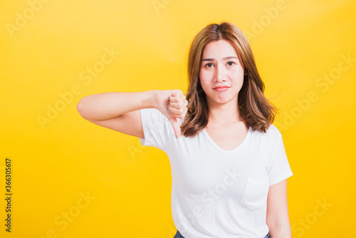 Portrait Asian Thai beautiful young woman unhappy, a negative gesture showing finger thumbs down or dislike sign, studio shot isolated on yellow background, There was copy space, rejection concept