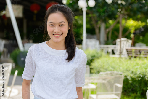 Happy young beautiful Asian woman smiling at the coffee shop outdoors